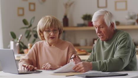 Senior-Couple-Going-through-Papers-and-Using-Laptop-at-Home